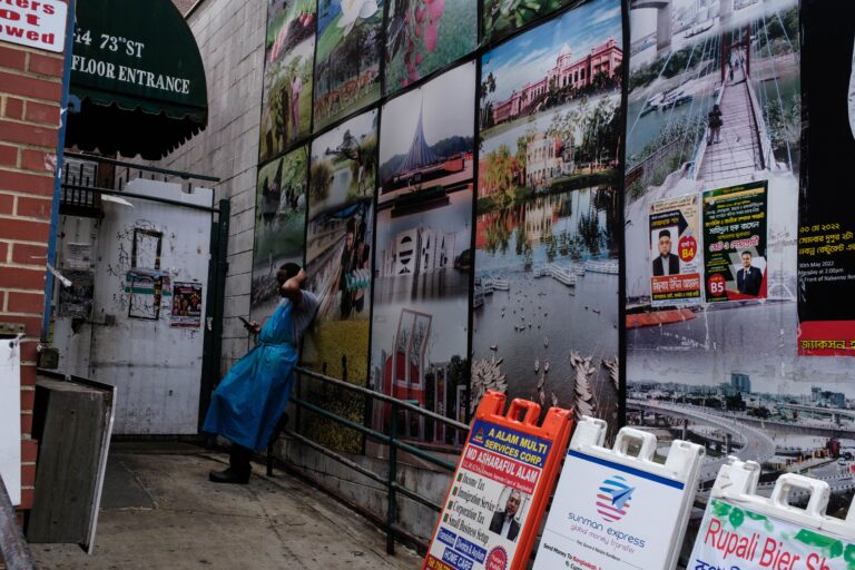 A restaurant employee takes a break with photographs of Bangladesh in the alley background. Jackson Heights, Queens, NY.